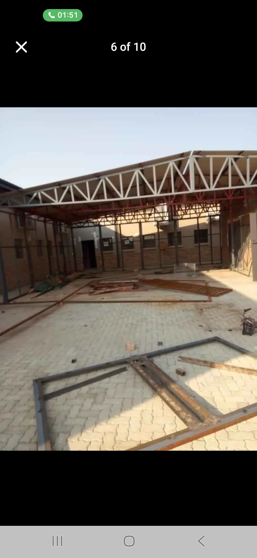 Metal roof truss structure under construction on a paved lot with scattered steel frames.