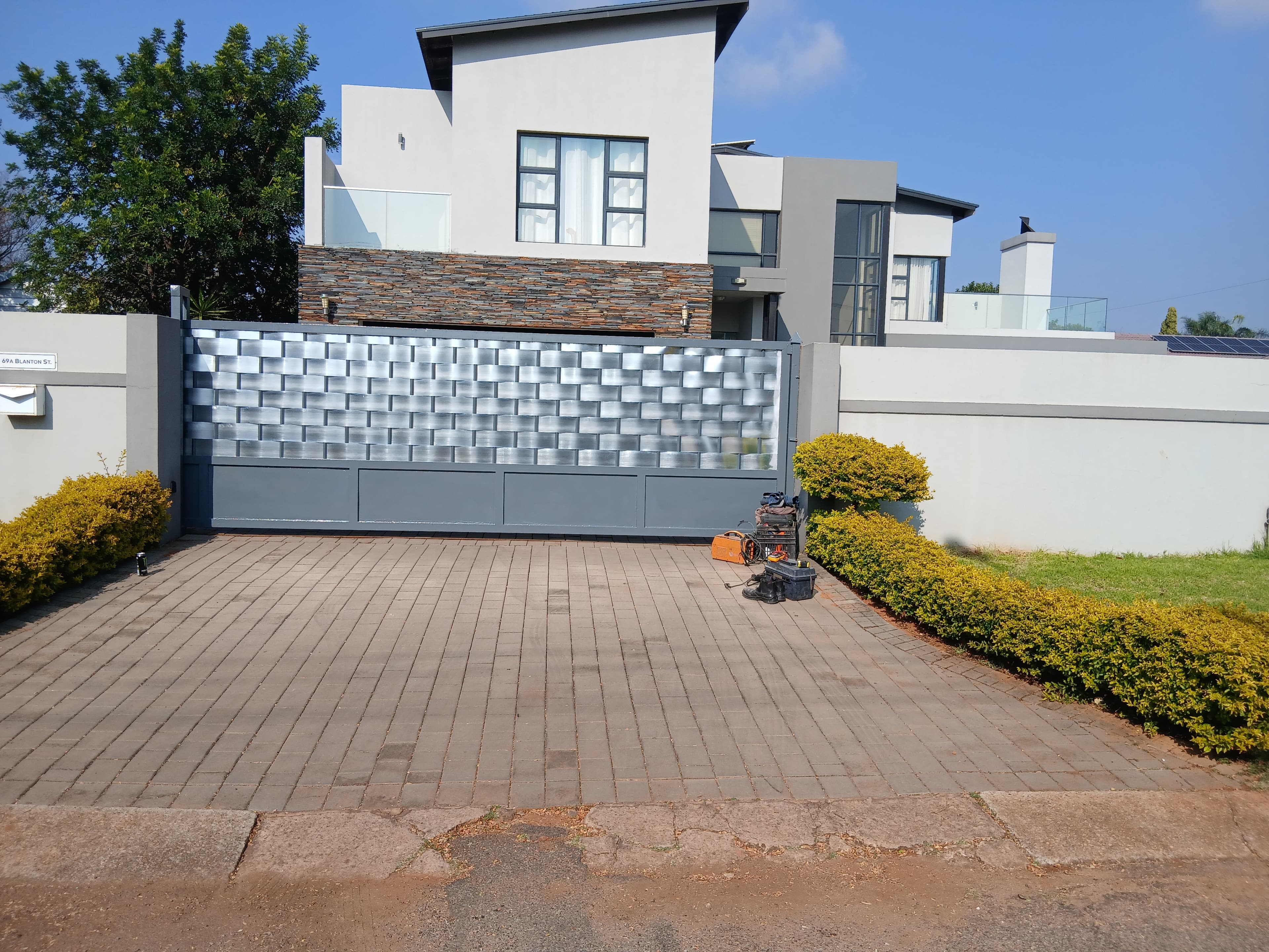 Modern house with a large grey textured metal gate and tools on the paved driveway.