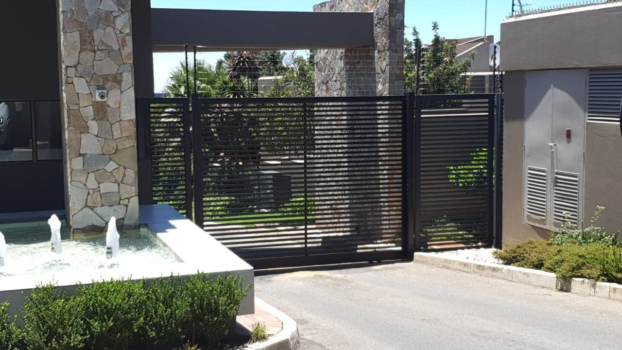 Black horizontal slat security gate between stone pillars with a small fountain in the foreground.