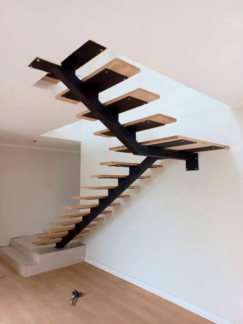 Modern floating staircase with black metal central spine and light wood treads in white room.